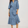 A woman modeling a blue and white vertically striped midi shirt dress with puff sleeves, a button-down front, and a tiered skirt, paired with black strappy heels against a plain white studio background.