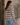A woman wearing a brown and cream plaid flannel shirt and light blue jeans, standing in profile next to a rustic wooden door with a potted plant in the background.
