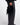 A person wearing black wide-leg leather pants, a black fuzzy top, and black pointed shoes holds a black fuzzy handbag with a small black pouch attached, photographed against a light gray studio background.