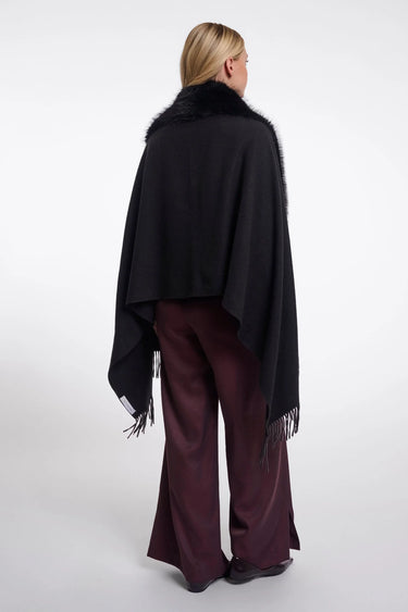 A woman shown from the back wearing a black shawl with dark fur trim over a burgundy wide-leg dress, photographed against a light gray studio background.