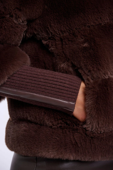 Close-up of a brown fur coat with a hand holding a brown leather wallet.