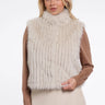 Woman wearing a beige fur vest over a brown long-sleeve top on a white background