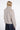 A model shown from the back wearing a light beige fuzzy cropped jacket with a high collar and a dark navy skirt, against a plain white studio background.