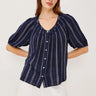 Woman wearing a navy striped blouse with white buttons and white shorts on a light background