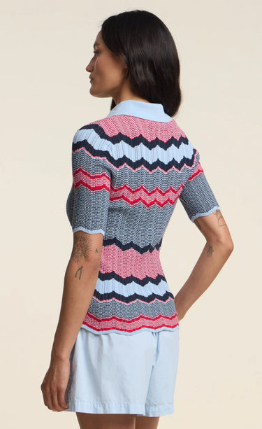 a woman wearing a zig zag stripe polo shirt with blue shorts on a neutral background