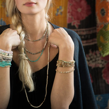Person wearing multiple necklaces and bracelets with a colorful background