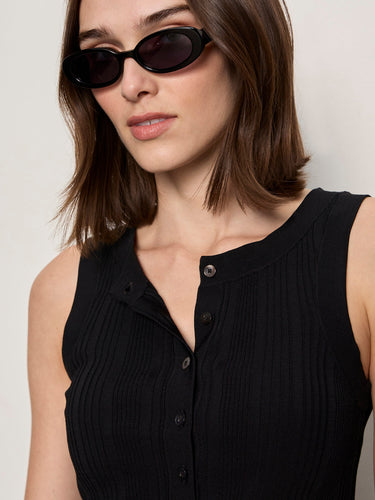a woman wearing a black henley tank top and blue pants on a white background