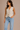 Woman wearing a beige ribbed vest and light blue jeans against a beige background