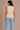 Woman wearing a beige sleeveless top and light blue jeans against a beige background