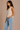 Woman wearing a beige sleeveless top and blue jeans against a beige background