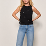Woman wearing a black sleeveless top with embellished front and blue jeans against a plain background