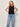 Woman wearing a black sleeveless top with embellished front and blue jeans against a plain background