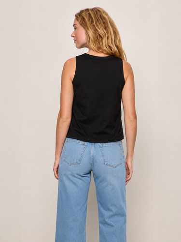 Woman wearing a black sleeveless top and blue jeans on a plain background