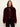 A woman modeling a plush, cropped fur jacket in deep burgundy. The jacket features a wide, high collar and is styled over a dark patterned top and black pants against a plain off-white studio background.