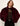 A woman wearing a plush, cropped burgundy faux fur jacket over a sheer black top and black pants, photographed against a plain off-white background.