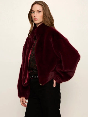 A woman modeling a plush, deep burgundy faux fur jacket with voluminous balloon sleeves, styled over a dark patterned top and black pants against a plain off-white background.