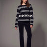 Black and white Fair Isle patterned sweater styled with slim black pants and black heels on a model.