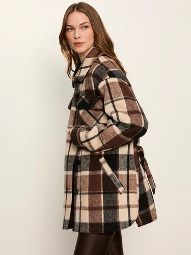A woman wearing a brown, beige, and black plaid coat, photographed from the side against a plain off-white background.