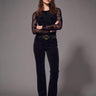 A woman wearing a black long sleeve floral mesh top and black pants on a grey studio background
