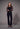 A woman wearing a black long sleeve floral mesh top and black pants on a grey studio background