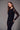 A woman wearing a black long sleeve floral mesh top and black pants on a grey studio background