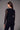 A woman wearing a black long sleeve floral mesh top and black pants on a grey studio background