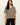 A woman modeling a short-sleeve knit sweater with horizontal beige and black stripes, paired with black pants, against a plain off-white background.
