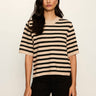 A woman modeling a short-sleeve knit sweater with horizontal beige and black stripes, paired with black pants, against a plain off-white background.