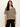 A woman modeling a short-sleeve knit sweater with horizontal beige and black stripes, paired with black pants, against a plain off-white background.