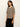 A woman modeling a short-sleeve knit sweater with horizontal beige and black stripes, paired with black pants, against a plain off-white background.