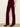 A model wearing deep burgundy corduroy flare jeans with black pointed-toe ankle boots, standing against a plain off-white wall.