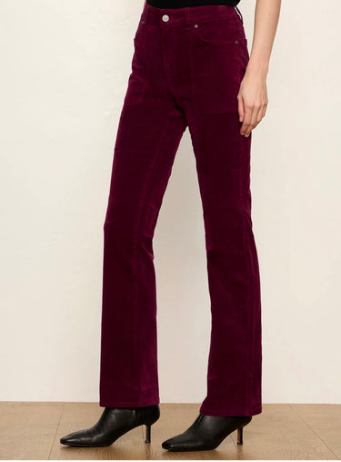 A model wearing deep burgundy corduroy flare jeans with black pointed-toe ankle boots, standing against a plain off-white wall.