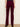 A person shown from the back wearing deep burgundy velvet flare pants with black high heels, standing against a plain off-white wall.