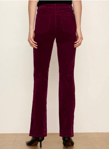 A person shown from the back wearing deep burgundy velvet flare pants with black high heels, standing against a plain off-white wall.