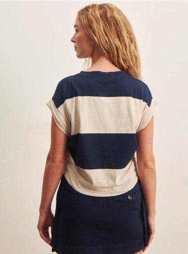A woman wearing a rugby-reminicient striped shirt in navy and opal with ruched side details and a navy blue skirt