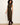 A woman modeling a sleeveless high-neck midi dress with a black and tan plaid pattern, paired with dark brown heeled boots, against a plain off-white studio background.