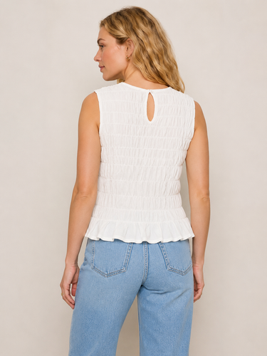 Woman wearing a white sleeveless top and blue jeans against a beige background