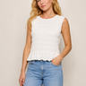Woman wearing a white sleeveless top and blue jeans against a beige background