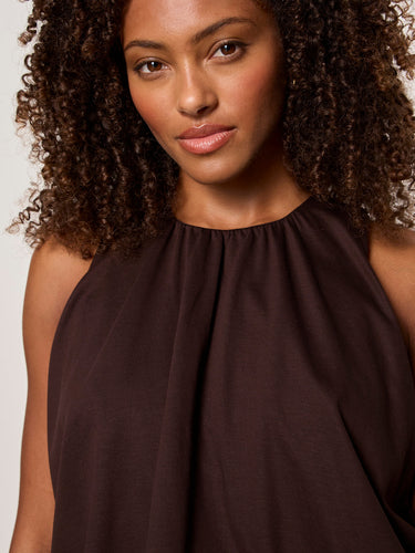 Woman wearing a brown sleeveless top against a neutral background