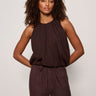 Woman wearing a brown sleeveless top and pants against a plain background