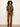 A model stands against a plain off-white wall wearing a brown and beige plaid button-up shirt with gold buttons and brown suede-like straight-leg pants.