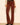A person wearing brown corduroy flared pants with a black belt, paired with a cream lace long-sleeve top and black pointed-toe heels, standing against a plain light beige wall.