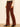 A person wearing brown corduroy flare pants with a black belt, paired with a cream lace long-sleeve top and black pointed-toe heels, standing against a plain off-white wall.