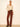 A model stands against a plain cream studio wall wearing a cream lace long-sleeve button-up shirt, brown corduroy flare pants with a black belt, and black pointed-toe heels.