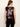 A woman shown from the back wearing a sleeveless sequined top with a deep V-neckline and black pants, set against a plain off-white background.