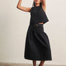 Woman wearing a black sleeveless top and black skirt with a belt against a plain background