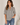A woman wearing a black and white vertically striped short-sleeve blouse with a split neckline, paired with blue jeans, standing against a light beige wall.