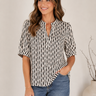 A woman wearing a black and white vertically striped short-sleeve blouse with a split neckline, paired with blue jeans, standing against a light beige wall.