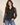 A woman modeling a black leopard-print button-up blouse with sheer long sleeves, paired with blue jeans, against a plain beige studio background.
