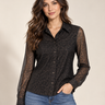 A woman modeling a black leopard-print button-up blouse with sheer long sleeves, paired with blue jeans, against a plain beige studio background.
